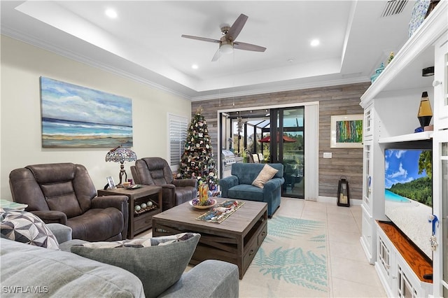 living room featuring a raised ceiling, wooden walls, ceiling fan, and light tile patterned floors