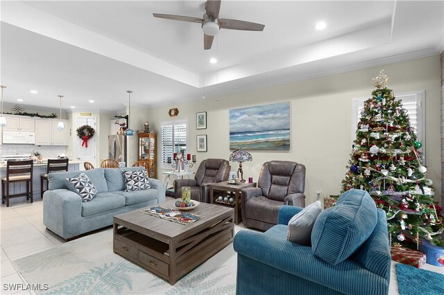 living room featuring light tile patterned floors, a tray ceiling, ceiling fan, and crown molding