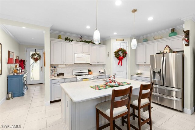 kitchen featuring ornamental molding, white appliances, decorative light fixtures, white cabinetry, and an island with sink