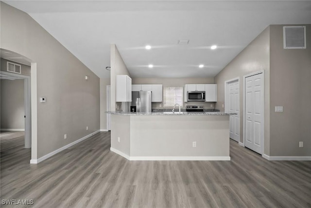 kitchen with appliances with stainless steel finishes, light stone counters, hardwood / wood-style flooring, white cabinetry, and lofted ceiling