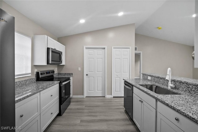 kitchen featuring appliances with stainless steel finishes, vaulted ceiling, sink, light hardwood / wood-style flooring, and white cabinetry