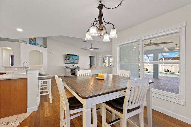 dining area featuring light wood-type flooring, vaulted ceiling, baseboards, and ceiling fan with notable chandelier