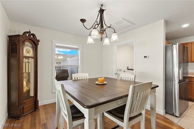 dining room with light wood-type flooring, visible vents, a chandelier, and baseboards