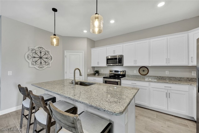 kitchen featuring appliances with stainless steel finishes, a center island with sink, white cabinetry, and hanging light fixtures