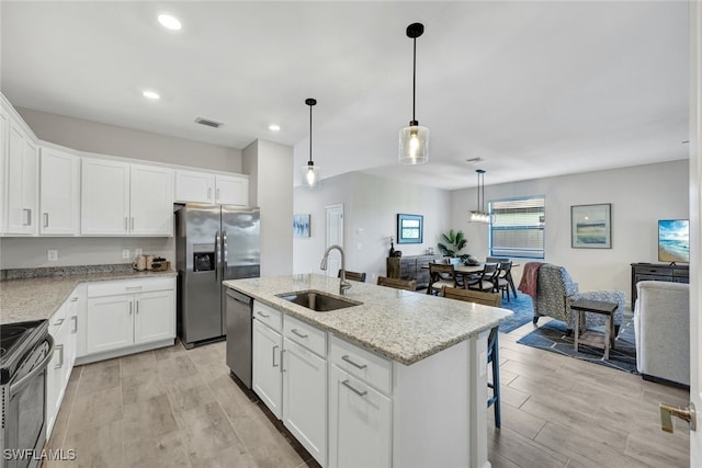 kitchen with a kitchen island with sink, hanging light fixtures, sink, white cabinetry, and stainless steel appliances