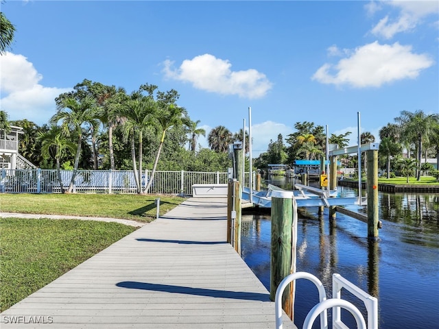 view of dock with a yard, fence, a water view, and boat lift