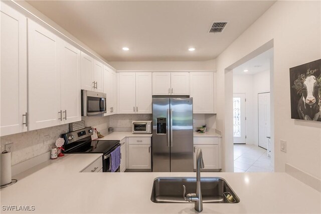 kitchen featuring white cabinets, sink, decorative backsplash, light tile patterned floors, and appliances with stainless steel finishes