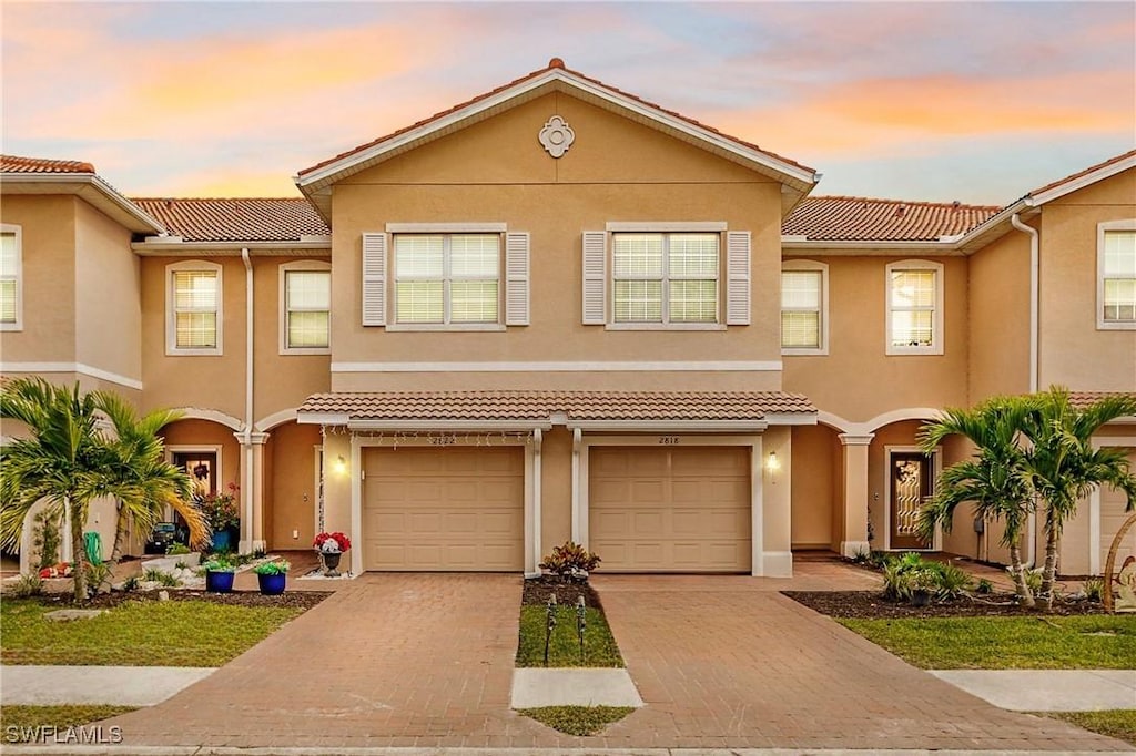 multi unit property with a tile roof, driveway, an attached garage, and stucco siding