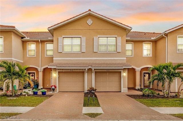 multi unit property with a tile roof, driveway, an attached garage, and stucco siding