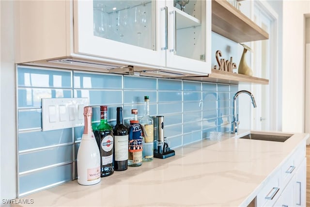 kitchen with sink, tasteful backsplash, white cabinetry, and light stone counters