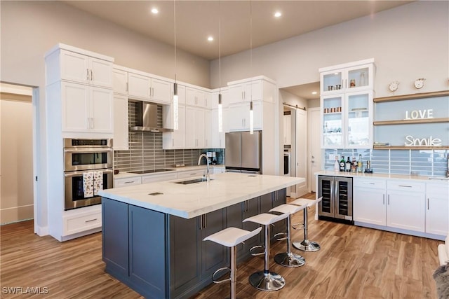 kitchen with appliances with stainless steel finishes, wall chimney exhaust hood, sink, white cabinets, and wine cooler