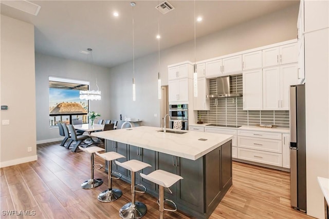 kitchen with wall chimney exhaust hood, white cabinetry, and an island with sink