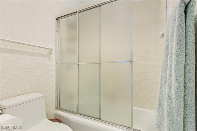 bathroom with toilet, tile walls, and shower / bath combination with glass door