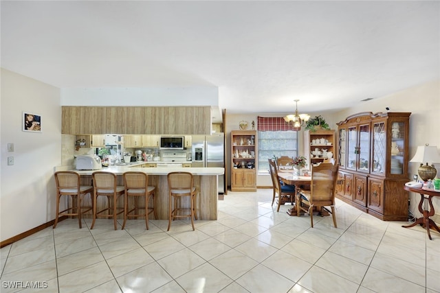 9940 Vanderbilt Dr, Naples, FL 34108 - kitchen featuring a peninsula, a chandelier, a kitchen bar, light countertops, and appliances with stainless steel finishes