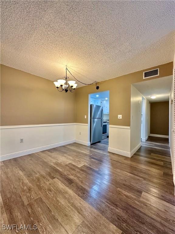 empty room with a textured ceiling, dark hardwood / wood-style floors, and a notable chandelier