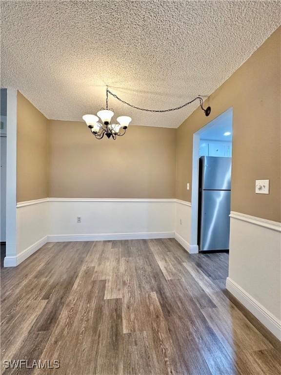 unfurnished dining area featuring hardwood / wood-style floors, a textured ceiling, and a chandelier