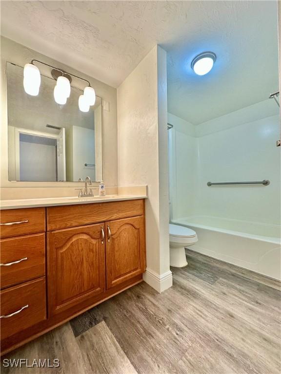 full bathroom with bathtub / shower combination, a textured ceiling, vanity, hardwood / wood-style flooring, and toilet