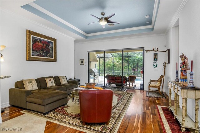 living room with ceiling fan, ornamental molding, a tray ceiling, and hardwood / wood-style floors