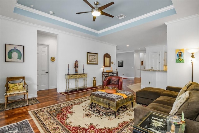 living room featuring ceiling fan, a tray ceiling, dark hardwood / wood-style floors, and crown molding