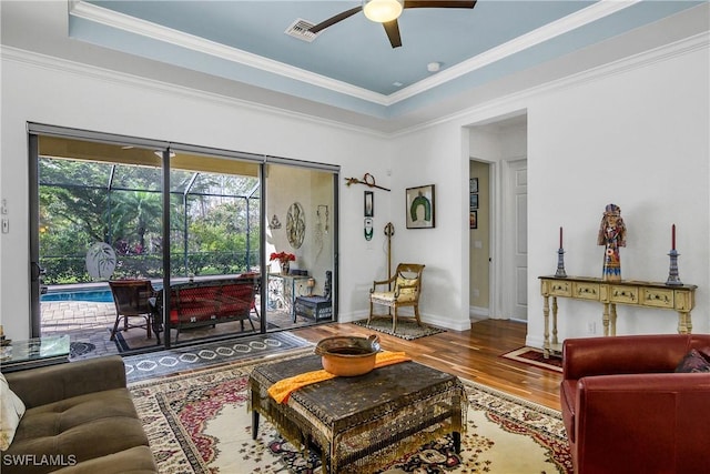 living room with a raised ceiling, crown molding, wood-type flooring, and ceiling fan