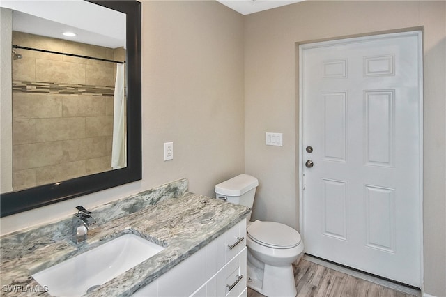 bathroom featuring tiled shower, toilet, vanity, and hardwood / wood-style flooring