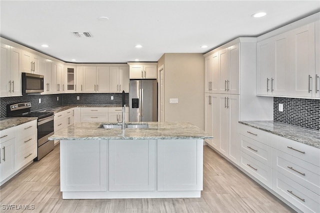 kitchen with sink, light hardwood / wood-style flooring, light stone countertops, an island with sink, and appliances with stainless steel finishes