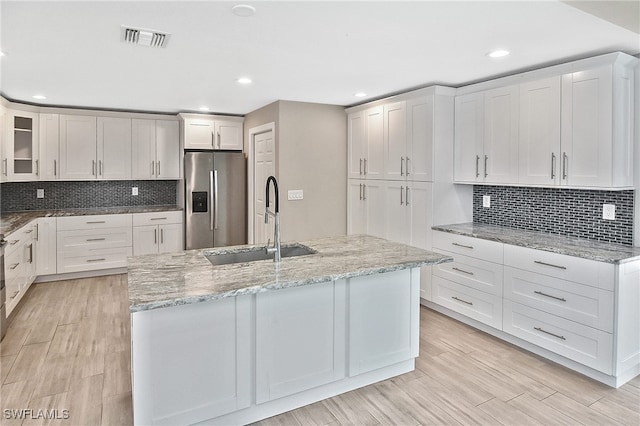 kitchen with stainless steel fridge, white cabinetry, a kitchen island with sink, and sink