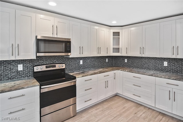 kitchen with tasteful backsplash, stainless steel appliances, dark stone countertops, light hardwood / wood-style floors, and white cabinetry