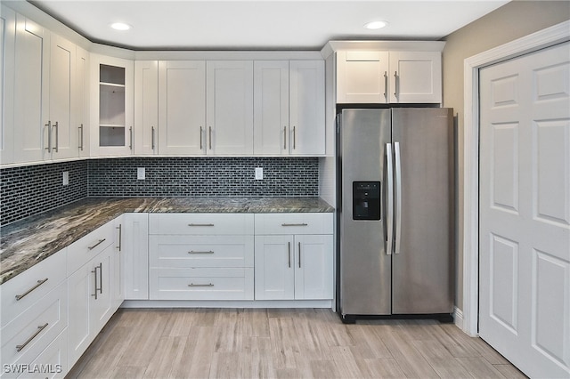 kitchen with dark stone counters, stainless steel refrigerator with ice dispenser, light hardwood / wood-style flooring, decorative backsplash, and white cabinetry