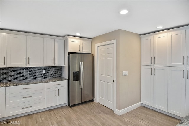 kitchen featuring dark stone counters, decorative backsplash, stainless steel fridge, light hardwood / wood-style floors, and white cabinetry