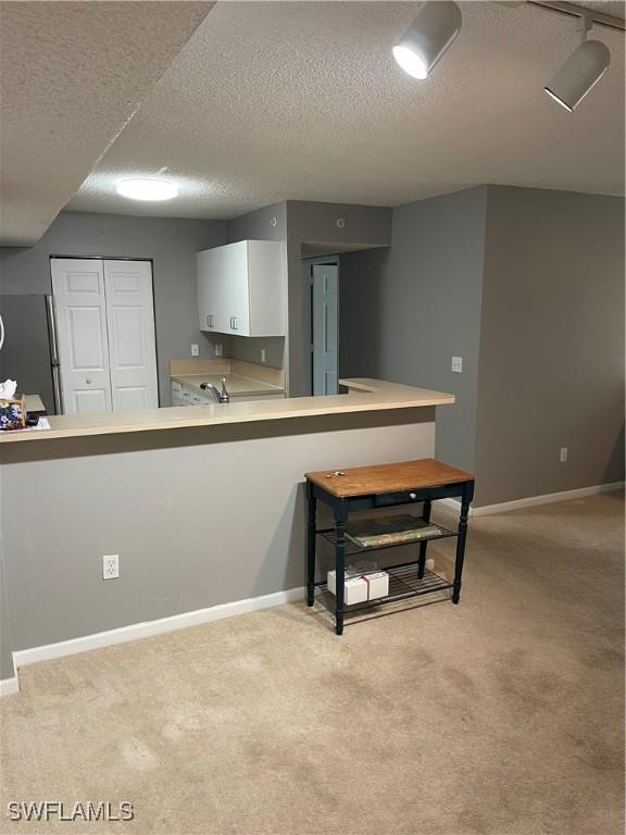 kitchen featuring stainless steel refrigerator, white cabinetry, light carpet, and a textured ceiling