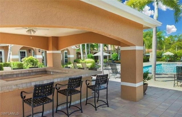 view of patio / terrace featuring ceiling fan, a community pool, and a bar