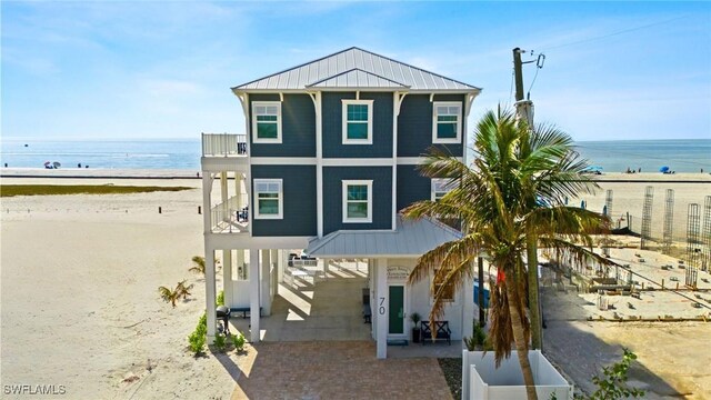 raised beach house with a carport, a water view, a beach view, and a balcony