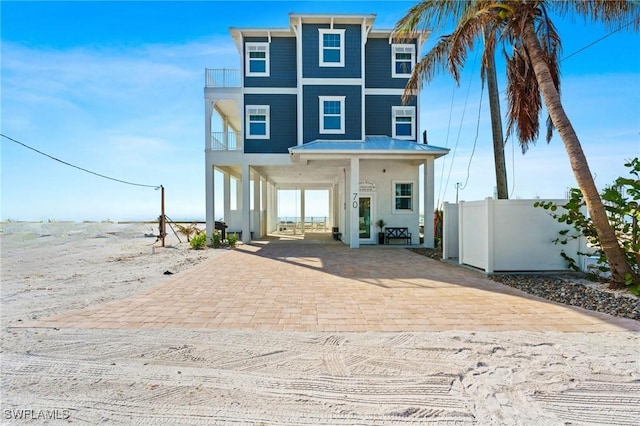 rear view of property featuring decorative driveway, fence, and a balcony