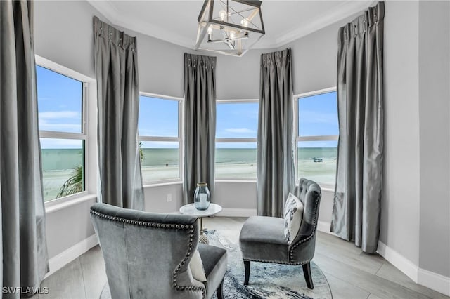 sitting room featuring a notable chandelier, light wood-style floors, a water view, and crown molding