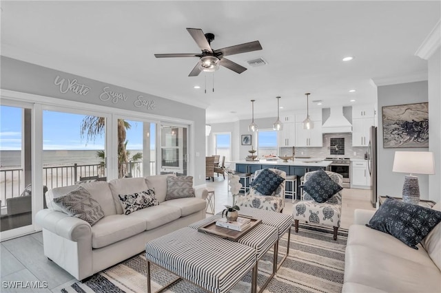 living room with recessed lighting, a water view, crown molding, and visible vents