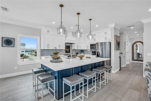 kitchen with decorative light fixtures, stainless steel appliances, white cabinets, light countertops, and a center island with sink