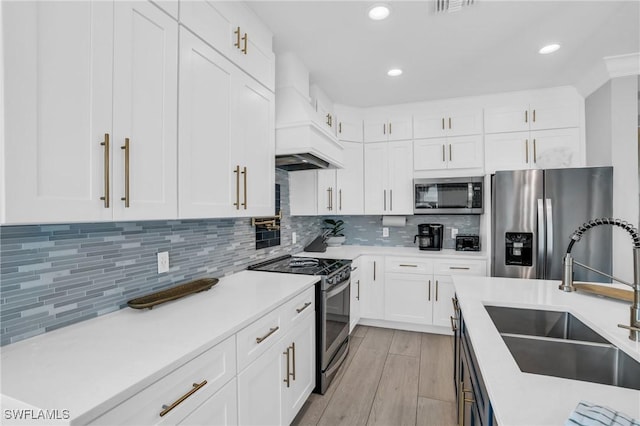 kitchen featuring custom exhaust hood, stainless steel appliances, light countertops, white cabinetry, and a sink