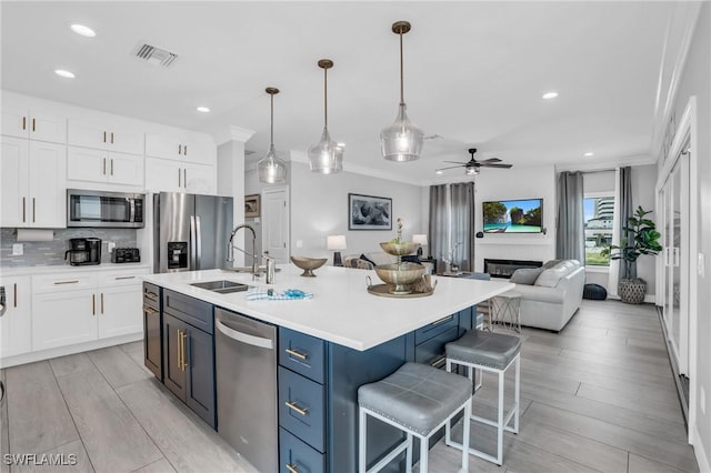 kitchen with appliances with stainless steel finishes, decorative light fixtures, light countertops, white cabinetry, and a sink