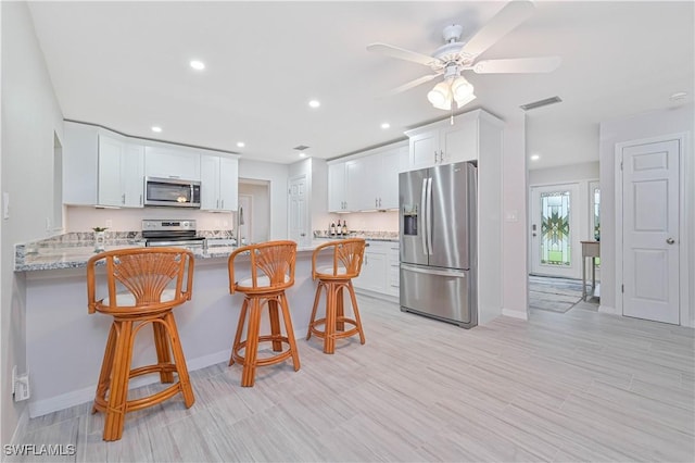 kitchen with light stone countertops, kitchen peninsula, a kitchen bar, white cabinets, and appliances with stainless steel finishes