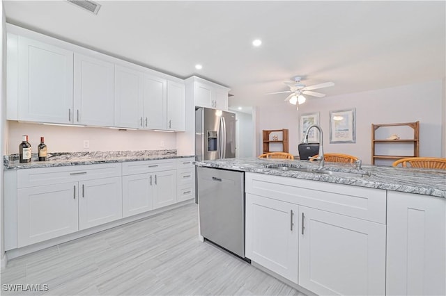 kitchen with white cabinetry, sink, ceiling fan, light stone counters, and appliances with stainless steel finishes