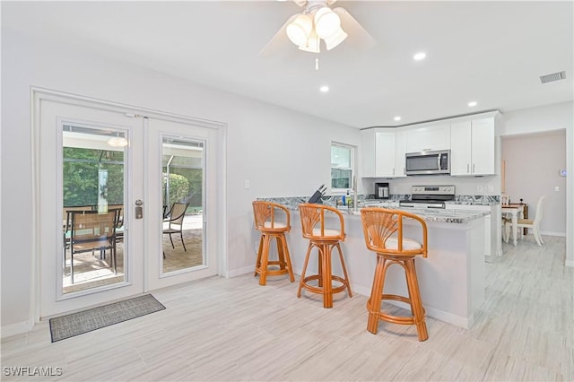 kitchen with kitchen peninsula, a kitchen breakfast bar, light stone countertops, stainless steel appliances, and white cabinets