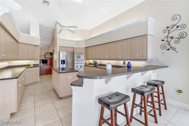 kitchen featuring white appliances, a towering ceiling, a kitchen island, kitchen peninsula, and a breakfast bar area