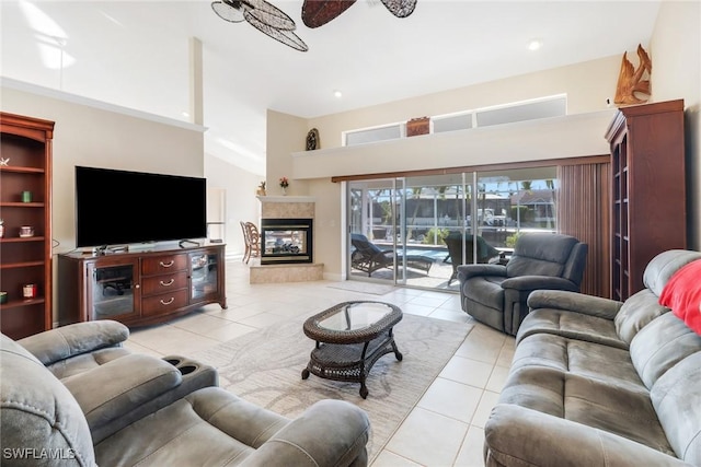 living room with light tile patterned floors, a towering ceiling, ceiling fan, and a tiled fireplace