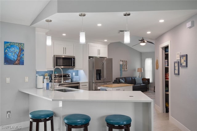 kitchen with lofted ceiling, kitchen peninsula, appliances with stainless steel finishes, white cabinetry, and a breakfast bar area