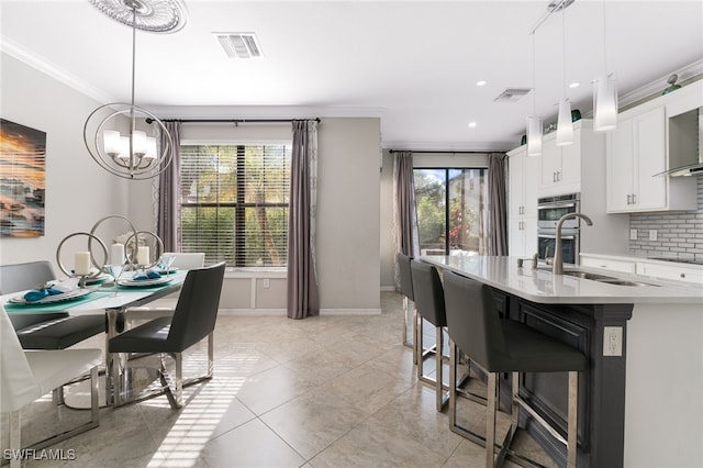 kitchen with a kitchen bar, ornamental molding, a kitchen island with sink, decorative light fixtures, and white cabinets