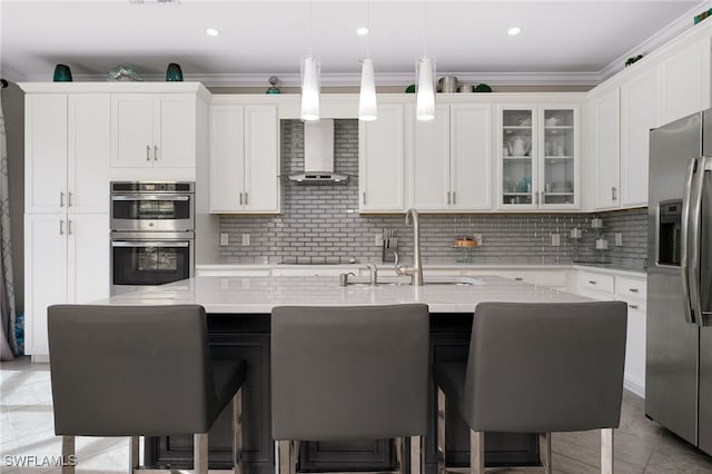 kitchen featuring wall chimney exhaust hood, a kitchen breakfast bar, an island with sink, and appliances with stainless steel finishes