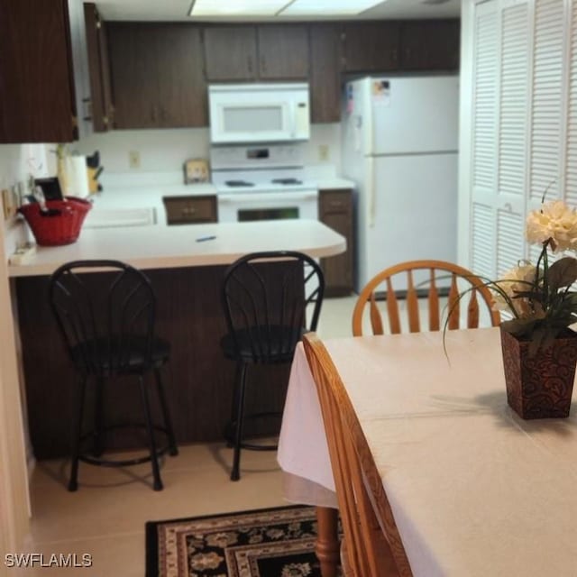 kitchen featuring a breakfast bar, dark brown cabinets, and white appliances