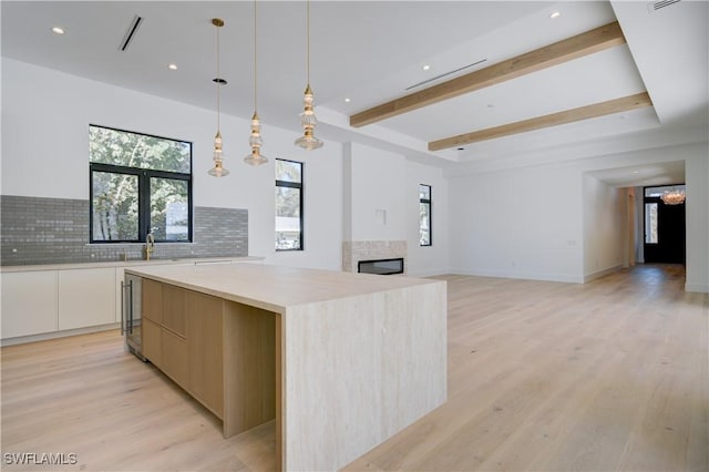 kitchen featuring pendant lighting, light hardwood / wood-style floors, white cabinets, a kitchen island, and decorative backsplash