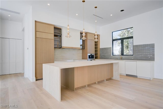 kitchen with a kitchen island, decorative light fixtures, white cabinetry, sink, and light hardwood / wood-style floors